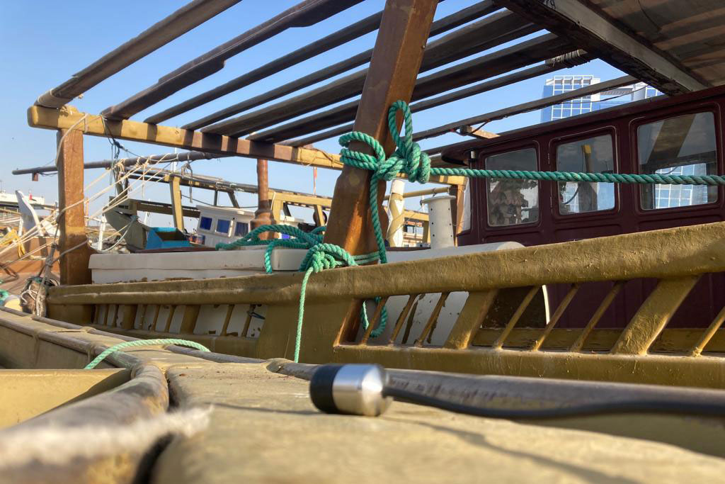 A microphone rests on the edge of a wooden dock or boat, alongside a boat tied up with turquoise rope.