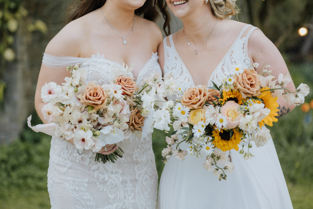 Brides wives smile hug laugh in garden holding bouquet of flowers daisies