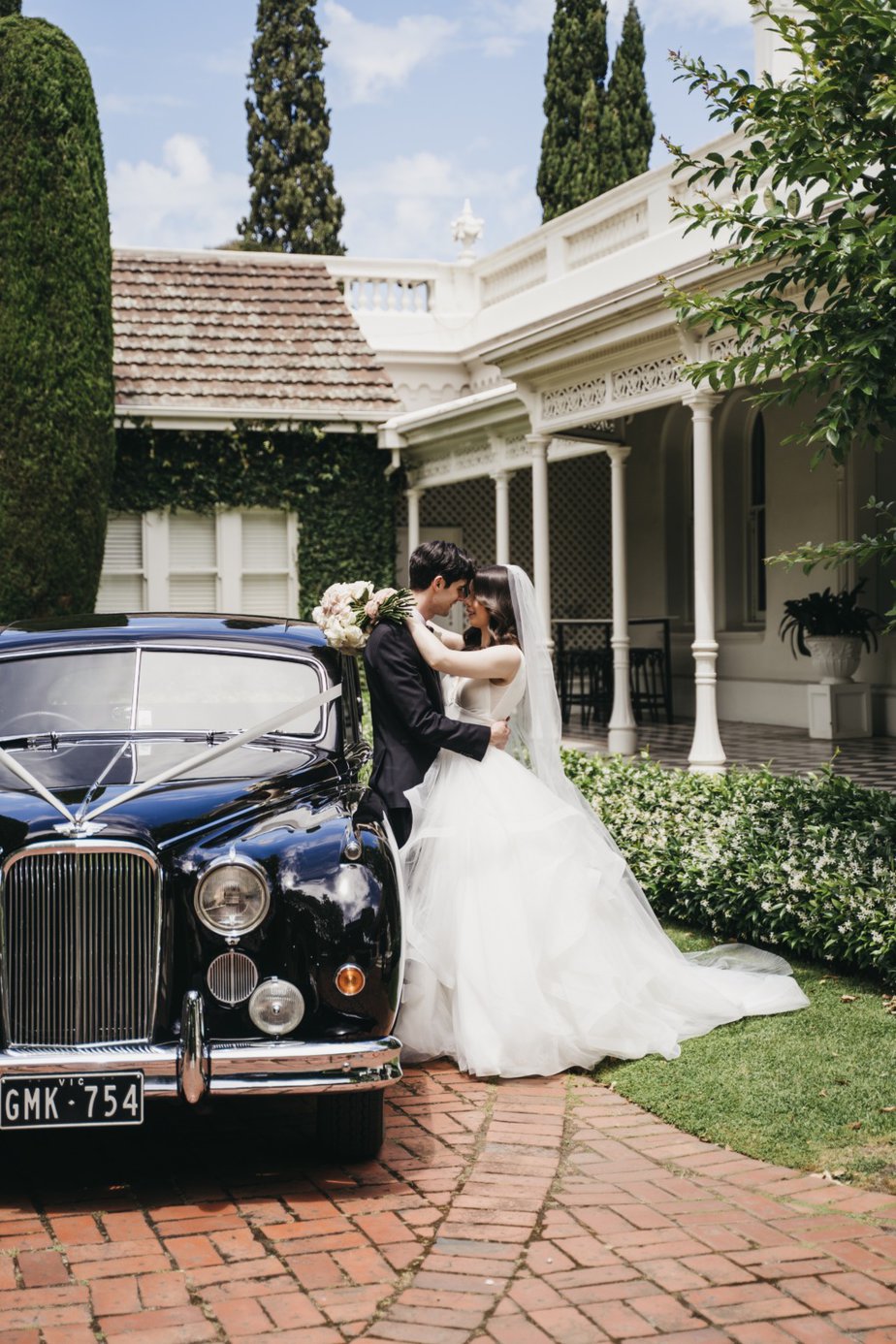 Bride and groom embrace beside wedding car