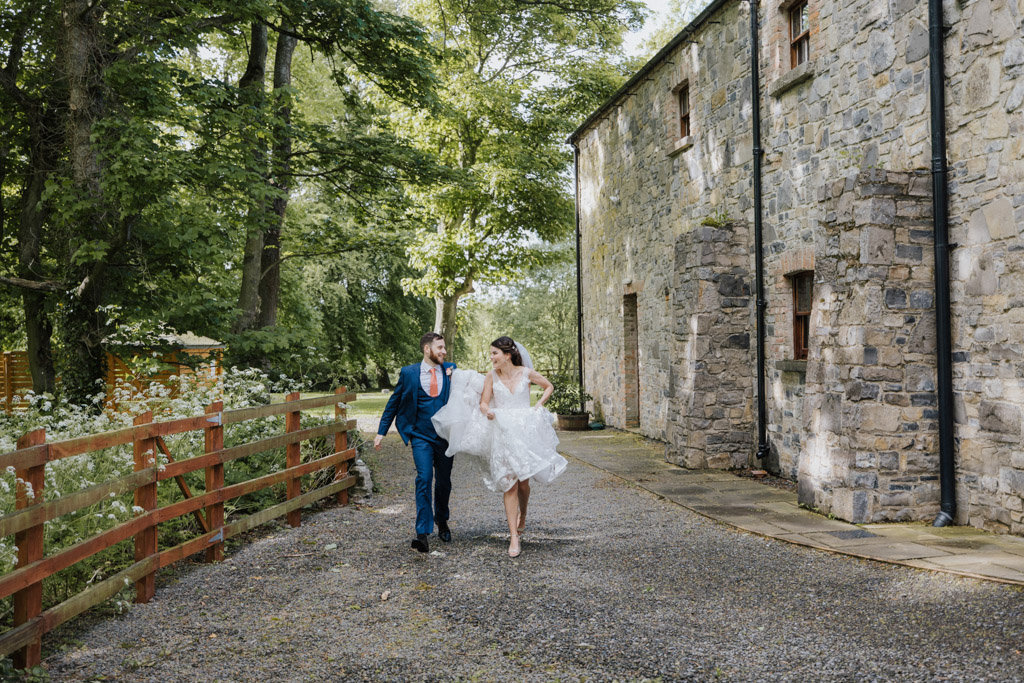Bride and groom walk towards camera holding bridal gown dress up