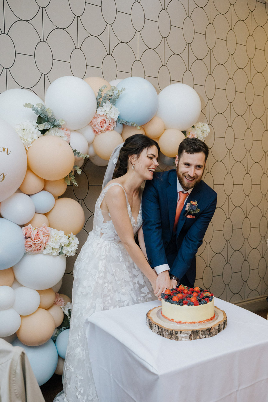 Pink and white balloons bride and groom cutting cake with strawberries on top