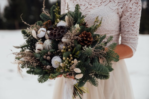 A winter bride holding a bouquet of evergreens and pinecones. 