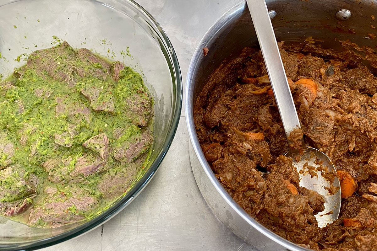 Two large bowls: one filled with meat marinading in a greenish sauce, and one with a finished meat stew, pieces of orange carrot visible, and a large silver serving spoon.