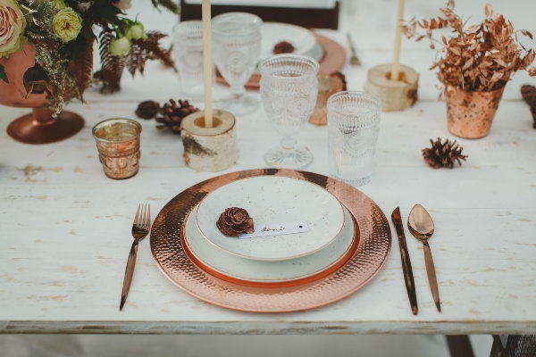 A table setting at a winter wedding with metallic dinnerware and pinecones. 