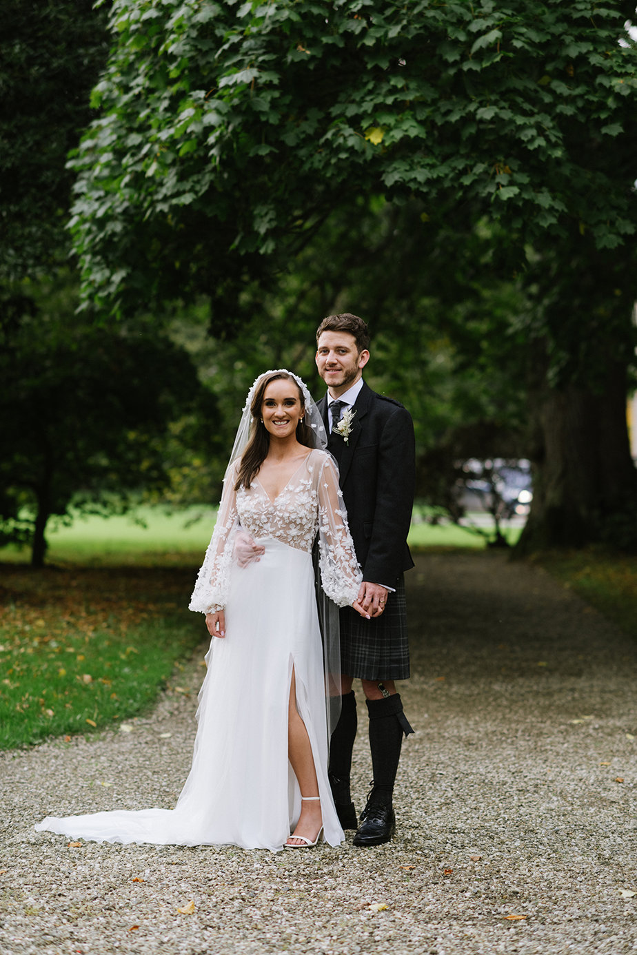 Bride and groom stand in garden park hand in hand holding hands