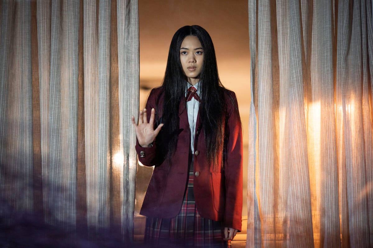 A young girl in a school uniform holds her hand up in a creepy way with dark wispy smoke covering the bottom half of the screen