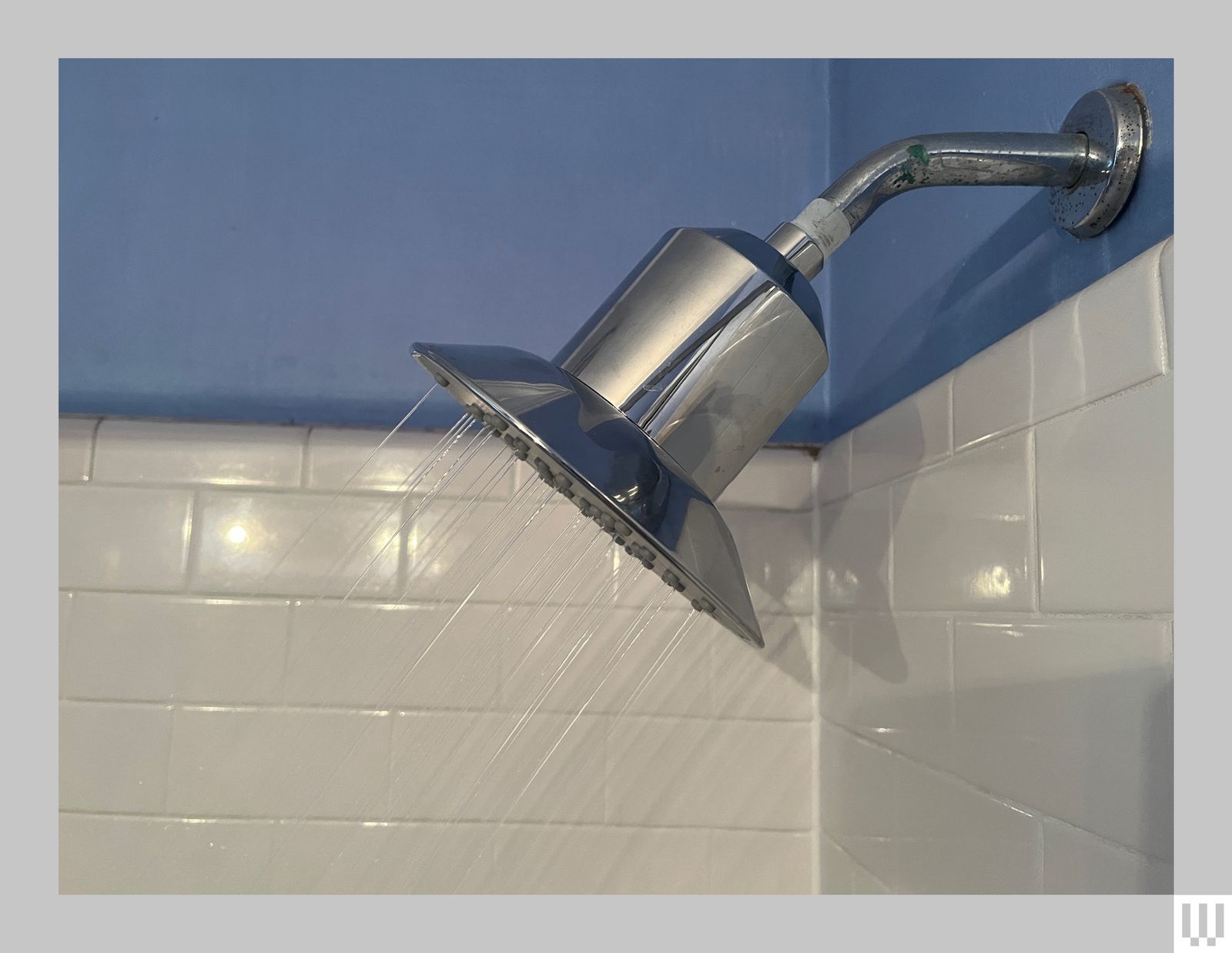 Silver bellshaped showerhead turned on with white tiles and blue walls in the background