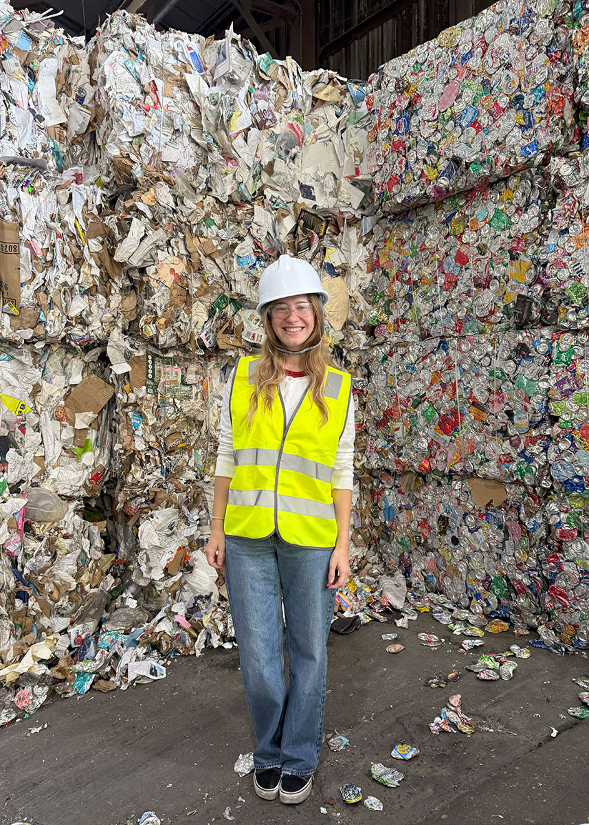 Woman in reflective safety vest standing in front of bales of compressed recycled material.
