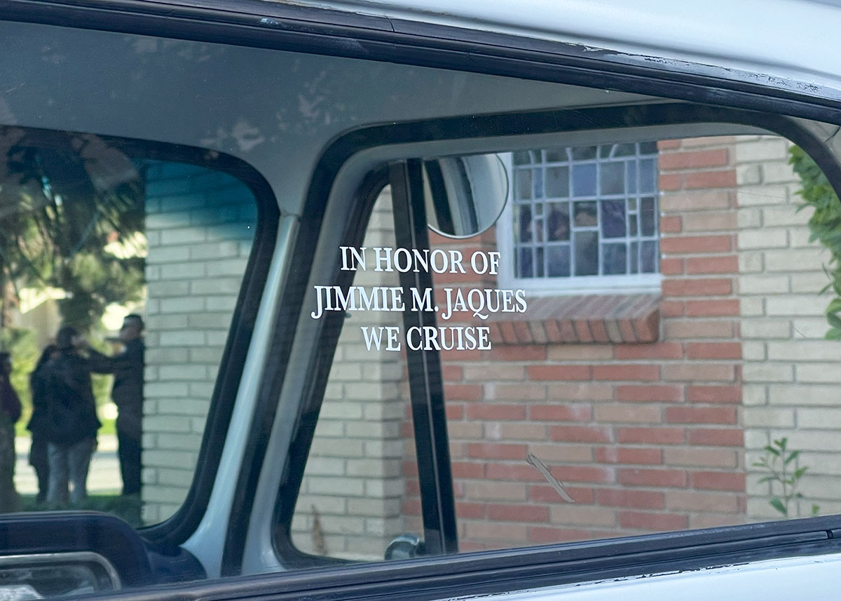 In the back windshielf of a classic truck, white letters read, In honor of Jimmie M. Jaques we cruise.