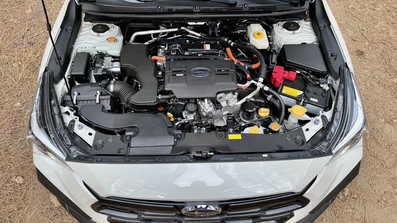 An underhood shot of the white Crosstrek Hybrid parked on pine needles