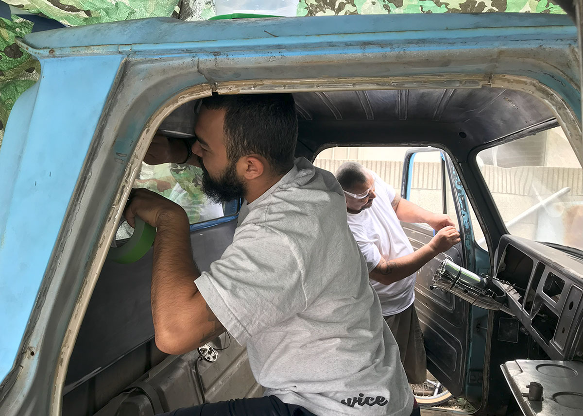 WIth both doors open, two men work on the interior of a turquoise truck.