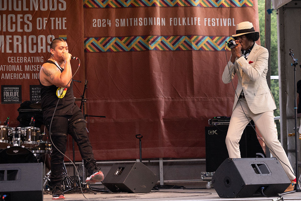 Two men, one in black and one in a white suit and fedora, perform on stage.