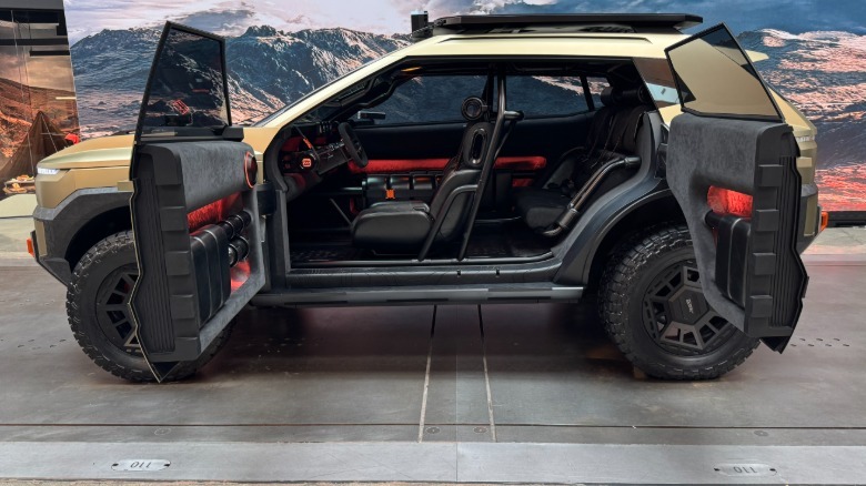 A wide side view of the Crater concept with its coach-style doors open parked in the XRT studio in front of a photo of mountains