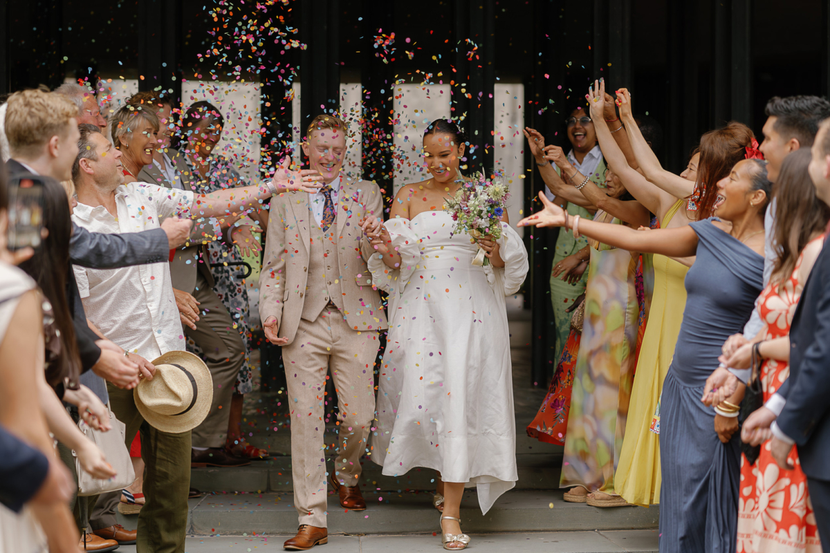 Amy & Tom's Stripped Back & Fun Tyne Bank Brewery Wedding 56 Bride and groom being showered with colourful paper confetti outside their registry office wedding in Newcastle upon Tyne. Bride wears gold block heel shoes with bow and an Aje dress. Silverbird Wedding Photography.