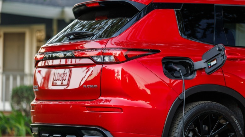 A rear side shot of the red Rogue PHEV with its charge port open and a plug in the socket