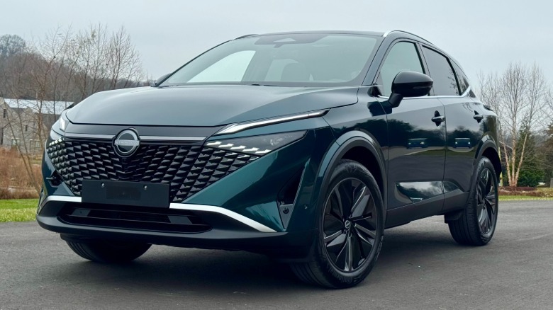 A front three quarters shot of a dark green Nissan Qashqai parked in front of bare trees and grass