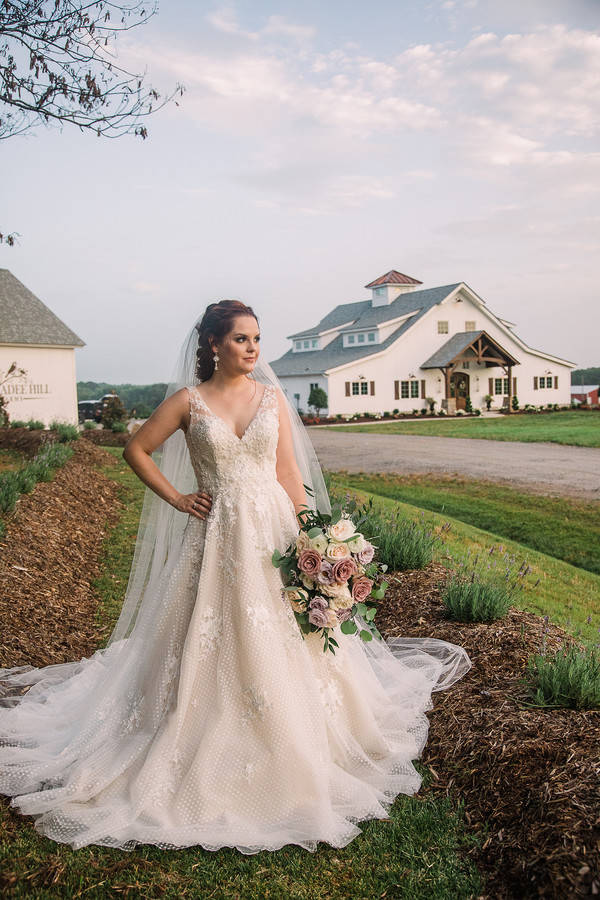 Bride in sleeveless V-neck ivory lace A-line gown with long cathedral train standing outdoors at Chickadee Hill Farm in North Carolina
