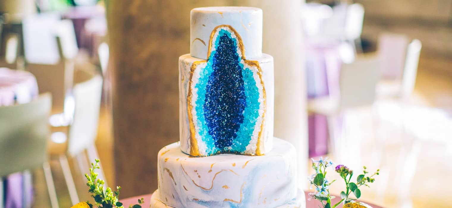 Wedding cake with a detailed blue and gold agate geode cross-section design, translucent crystal layers on a white marble base tier