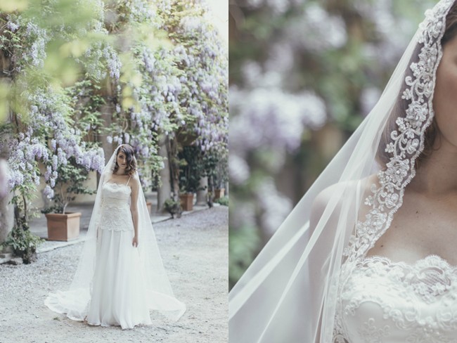 Bride in 1920s drop-waist chiffon and lace gown with white gloves under wisteria blooms in a Milan courtyard