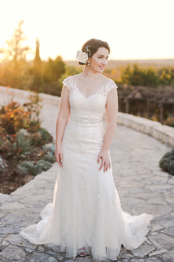 Bride in fitted lace wedding gown with cap sleeves and beaded belt at golden hour outdoors