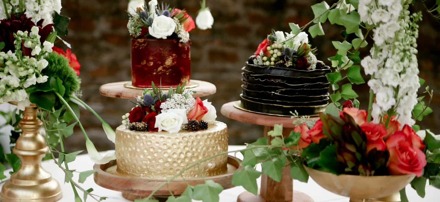 Black wedding cake tier with deep red roses and dark berries on a gold cake stand, styled with lush dark florals