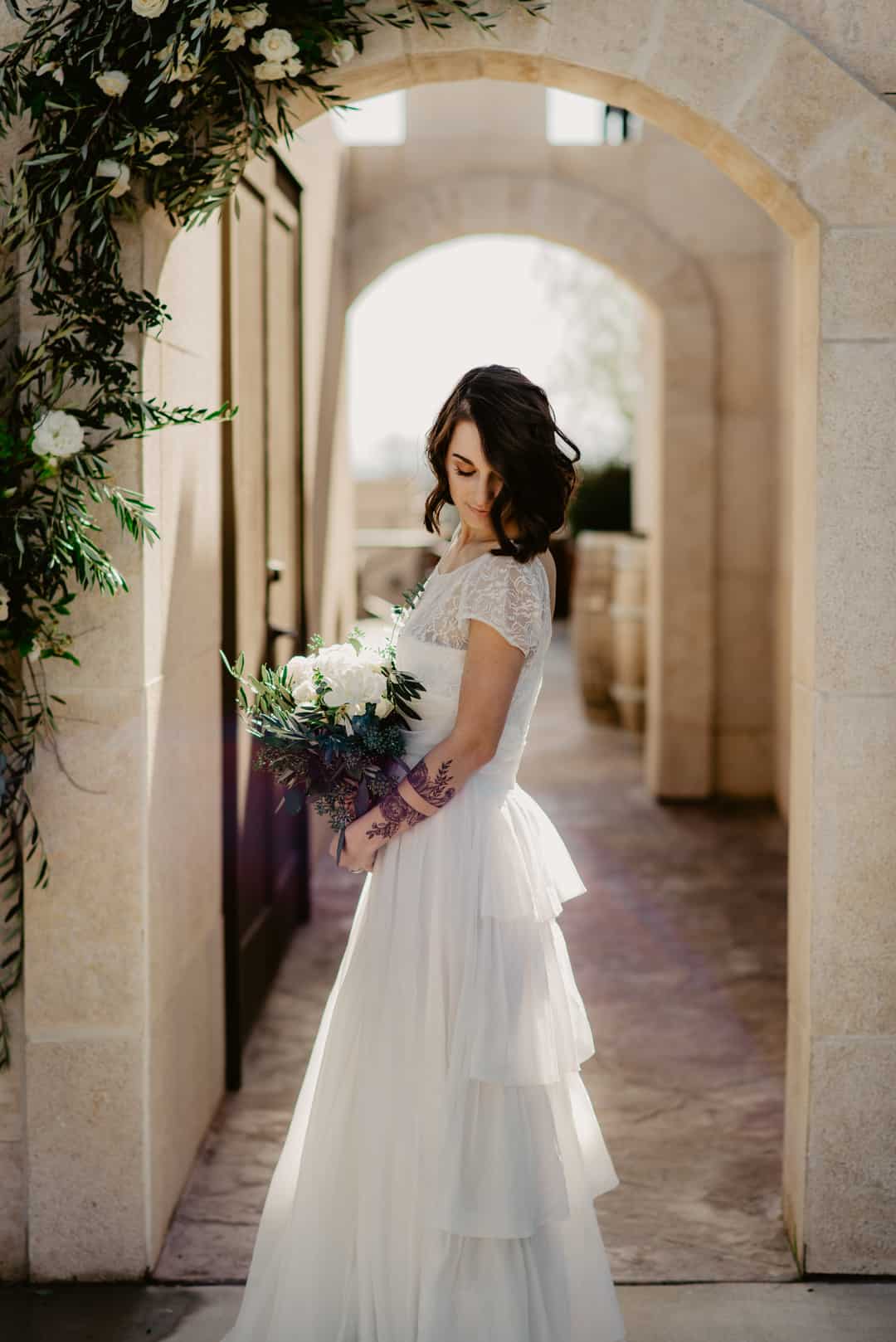 Bride in short-sleeve white lace and tulle A-line gown holding bouquet at Tooth and Nail Winery in Paso Robles, California