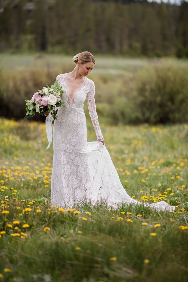Bride in long-sleeve deep V-neck ivory lace wedding gown standing in wildflower meadow in Colorado