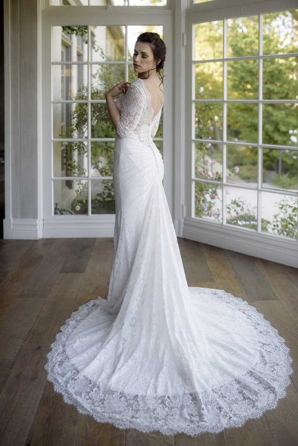 Back view of bride in sleek boat-neck lace sheath gown showing dramatic circle train with scalloped lace hem at Malibou Lake Lodge