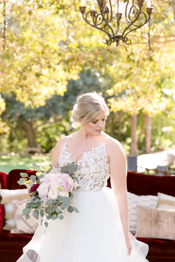 Plus-size bride in white ball gown with V-neckline, spaghetti straps, lace bodice, and full tulle skirt standing outdoors under a chandelier