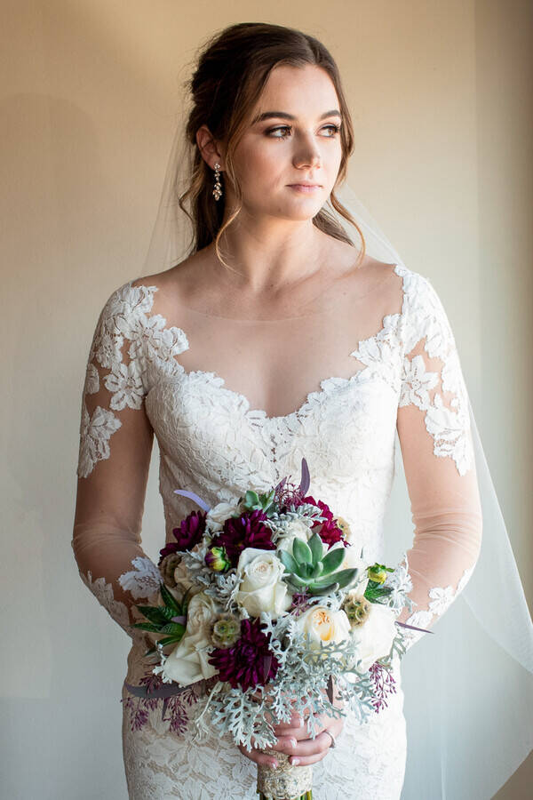 Bride Halley in a long-sleeve illusion lace mermaid gown with scalloped sweetheart neckline, holding a burgundy dahlia and succulent bouquet, at Mighty Tieton in Tieton, Washington