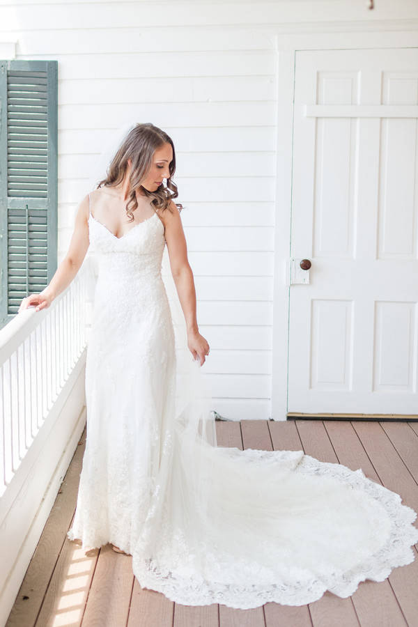 Bride in spaghetti-strap lace sheath gown with dramatic scalloped circle train on porch at The Antrim 1844