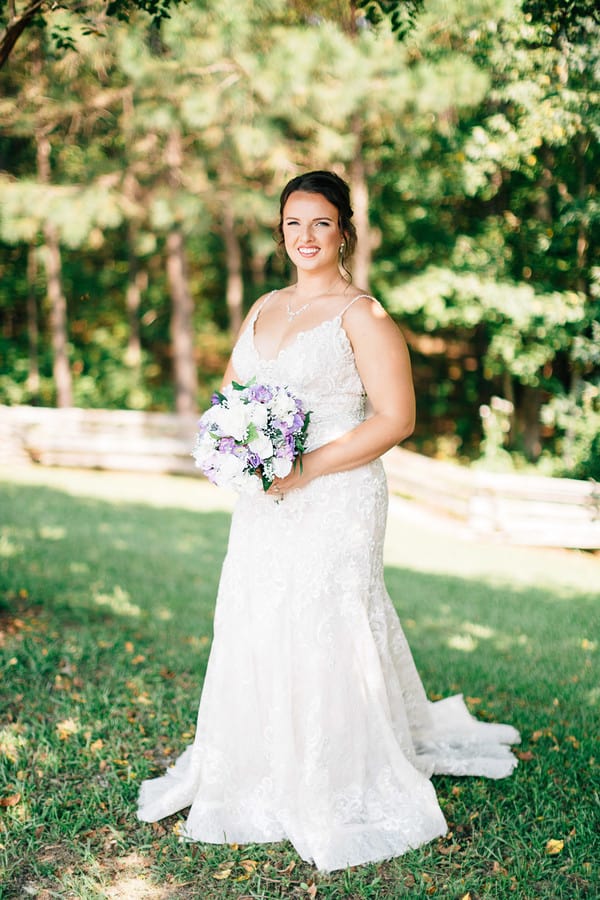 Plus-size bride in full-length white lace fit-and-flare gown with spaghetti straps and V-neckline standing in a garden setting