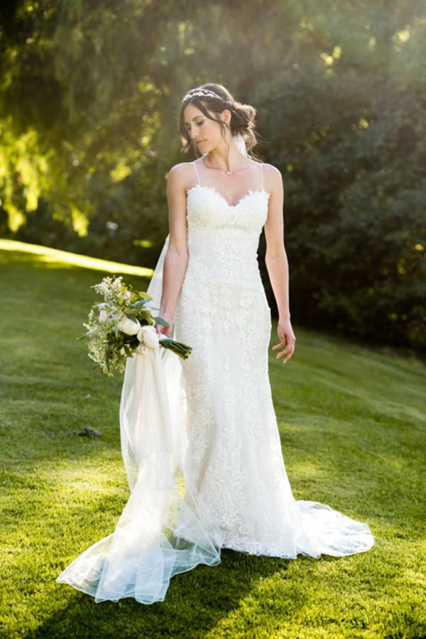 Bride in spaghetti-strap floral lace sheath wedding gown with sweetheart neckline standing in garden at Temecula Creek Inn