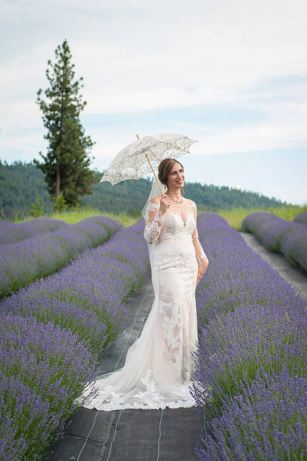 Bride in ivory off-shoulder lace mermaid gown posing in lavender field with lace parasol in Spokane, Washington