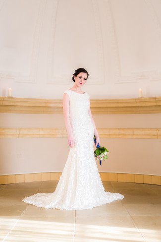 Bride in boat-neck cap-sleeve fitted lace sheath gown standing under the dome of Normanton Church at Rutland Water in England
