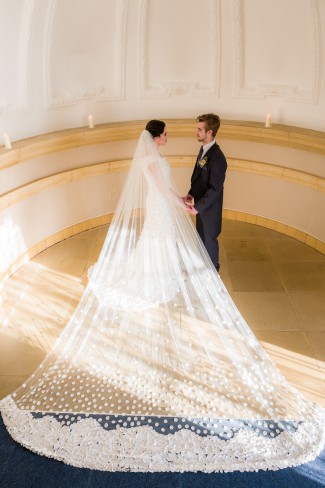 Bride in cap-sleeve white lace sheath gown with cathedral veil spread dramatically across church floor at Normanton Church, England