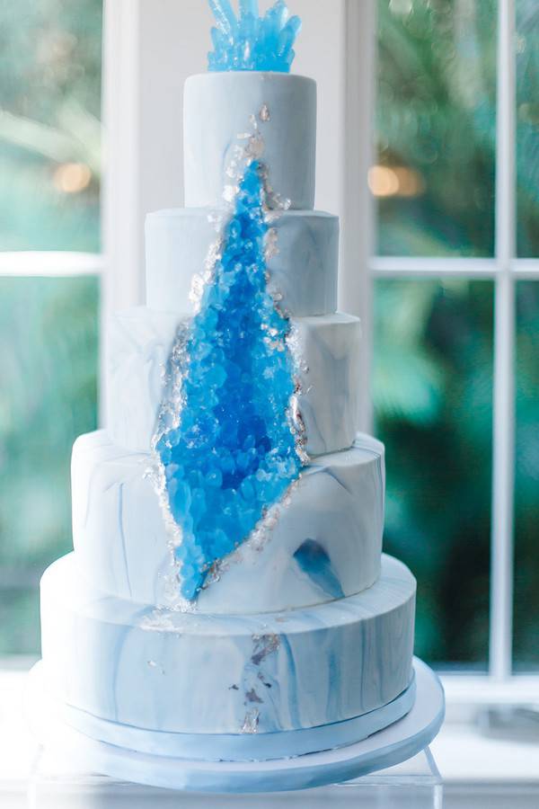 Five-tier white and grey marble wedding cake with a dramatic blue crystal geode formation and ice effect through the center tiers