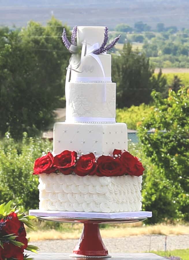 Five-tier white fondant wedding cake topped with large red roses and lavender sprigs, simple and tall with a statement custom topper