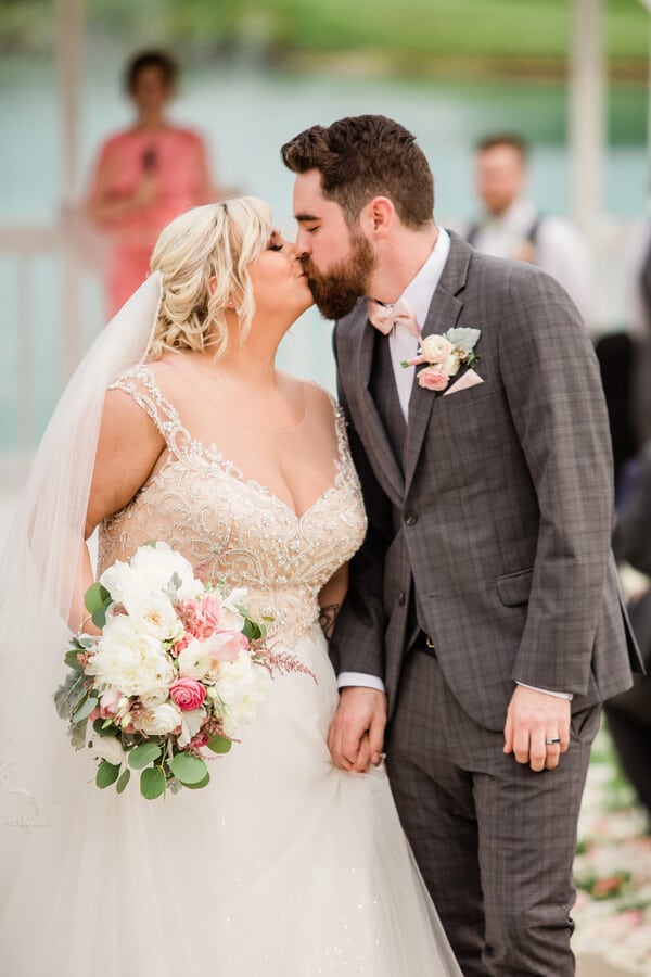 Bride in white cap-sleeve sweetheart ball gown with lace and tulle kissing groom at the altar during ceremony