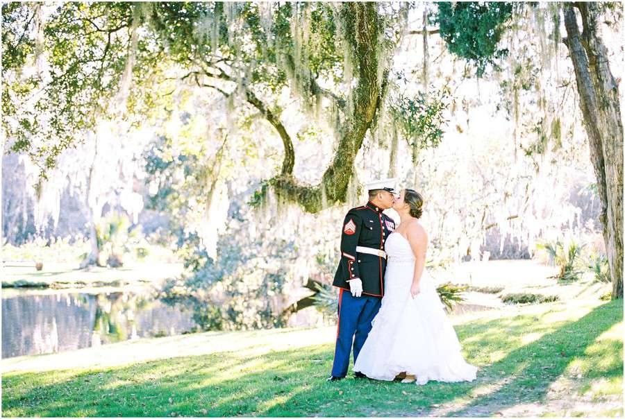 Bride in white strapless floor-length wedding gown kissing groom under Spanish moss trees at a lakeside in Charleston
