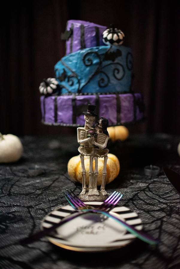 Three-tier dark wedding cake with colorful painted details and a skeleton bride and groom fondant topper in Nightmare Before Christmas style