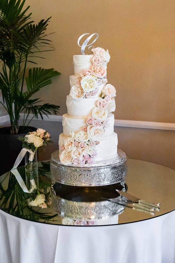 Five-tier tall white fondant wedding cake with cascading fresh or sugar flowers flowing from top to base in soft white and blush tones