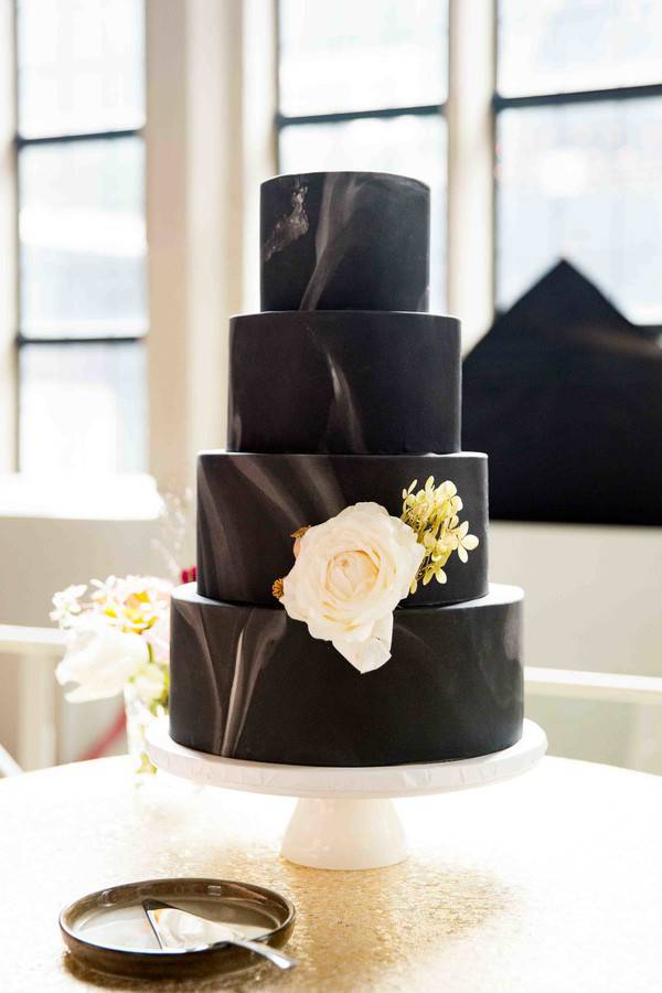 Four-tier black and white marble fondant wedding cake with a single large cream rose, elegant and modern