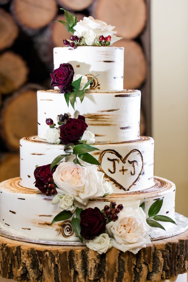 Four-tier fondant wedding cake with realistic birch wood bark texture and cascading peach, ivory, and blush flowers