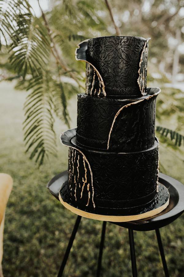 Three-tier black and gold marble wedding cake with raised embossed floral details and gold leaf accents