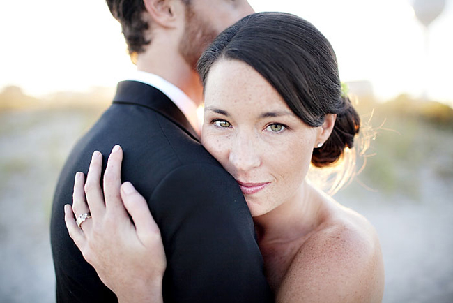 Bride resting her cheek on the groom's chest with her hand on his shoulder, looking at the camera