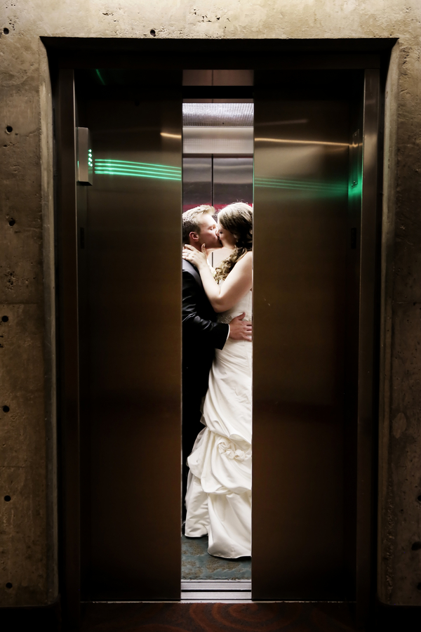 Couple kissing inside an elevator framed by partly open metal doors