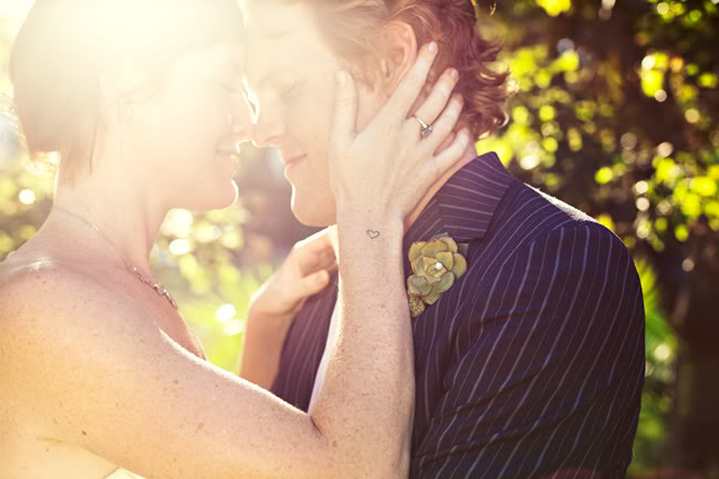 Backlit couple with foreheads pressed together, the bride's hand on the groom's cheek