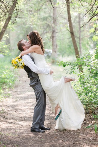 Groom lifting the bride off the ground into a kiss on a wooded path, her bouquet flowing
