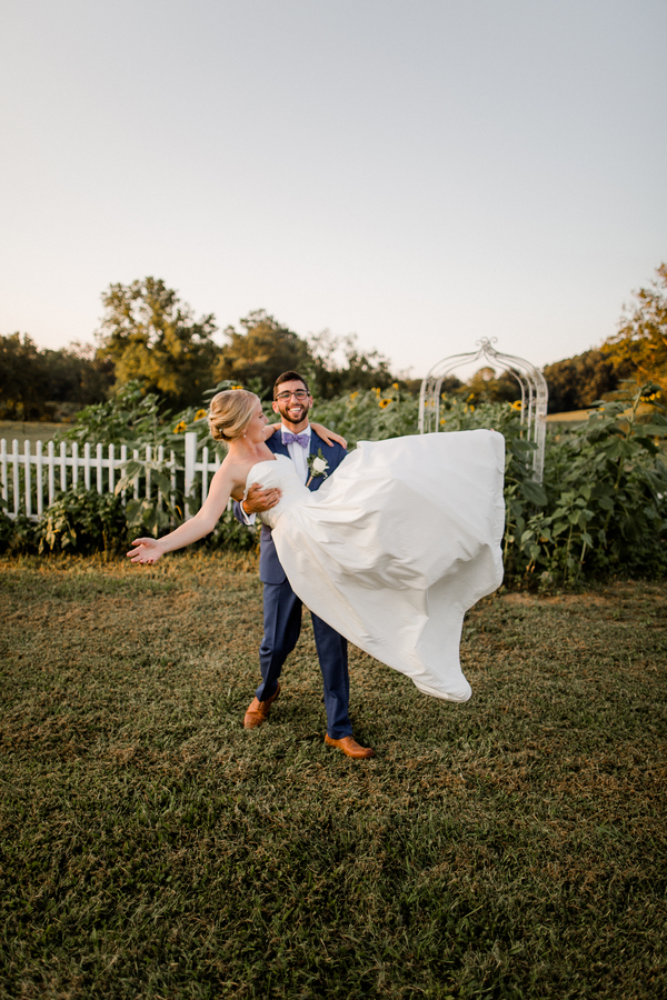 Groom carrying the bride in his arms, her dress flaring, as he walks